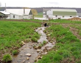 A rocky stream approaches some farm buildings in the center County Conservation District.